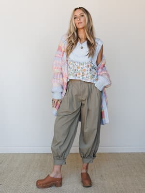 A relaxed, layered look built around olive barrel pants styled with a floral crop top, pastel multicolor knit cardigan, and wood-studded clogs — the kind of outfit that looks effortless but was definitely thought about.