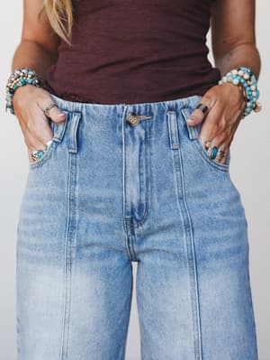 A close-up detail shot of light wash wide-leg jeans styled with a deep burgundy tank and stacked turquoise and silver jewelry — the kind of effortless outfit that looks like it took two minutes but absolutely didn't.