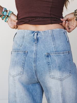 A close-up back view of light wash wide-leg jeans paired with a cropped burgundy top, styled with stacked turquoise and beaded bracelets — the kind of effortless denim moment you want to recreate every weekend.