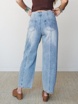 A back-view shot of wide-leg light wash jeans styled with a cropped dark top and brown platform clogs — relaxed, lived-in denim with a retro ease that works just as hard for a coffee run as it does for a night out.