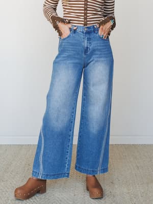 Wide-leg denim jeans styled with a brown striped long-sleeve top and wood-stacked clogs — a 70s-leaning, lived-in look that feels effortless without trying.
