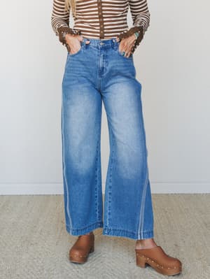 Wide-leg medium-wash jeans styled with a brown striped cropped top and brown clogs — a 70s-leaning, effortlessly cool outfit with turquoise jewelry doing all the right things.