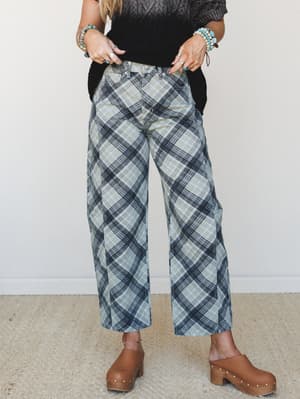 Wide-leg plaid pants in a muted sage and navy mix, styled with a black knit top and brown studded clogs — the kind of outfit that looks effortless but very much on purpose.