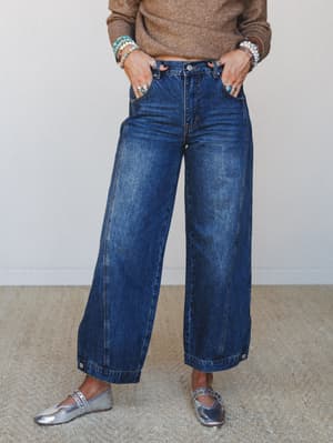 Wide-leg dark wash jeans styled with a camel knit sweater, stacked turquoise and stone bracelets, and silver metallic flats — the kind of effortless outfit that looks like it came together in five minutes but took real thought.
