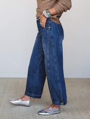 A side-profile shot of wide-leg cropped denim jeans styled with a camel sweater, silver mary jane flats, and a stack of turquoise and pearl bracelets — the kind of outfit that looks effortless but was definitely thought about.