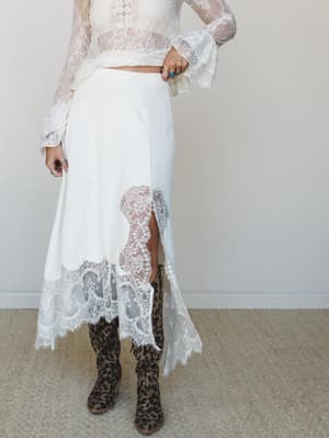 A cream lace-trimmed midi skirt paired with a sheer lace bell-sleeve crop top and leopard print cowboy boots — the kind of outfit that walks into a backyard wedding and makes everyone ask where you got it.