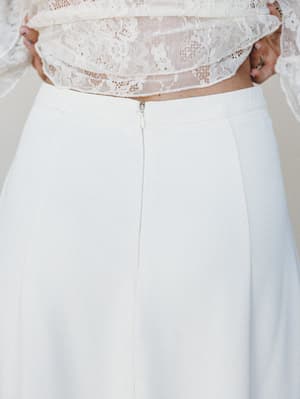 A close-up detail shot of a cream midi skirt styled with a floral lace crop top, shot from behind to highlight the back zipper closure and clean A-line silhouette — soft, romantic, and bridal without trying too hard.