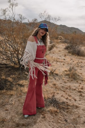 Woman in red overalls and white top standing in a desert landscape
