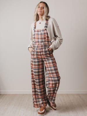 Woman wearing plaid overalls and a light-colored sweatshirt against a plain background