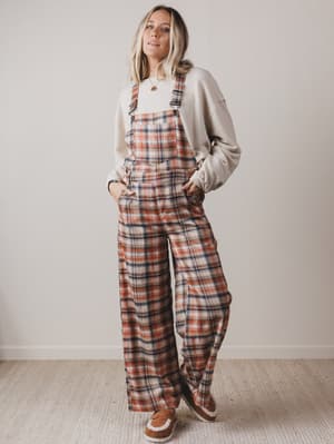 Woman wearing plaid overalls and a light-colored sweatshirt against a plain background