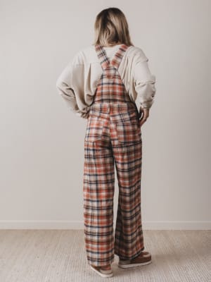 Person wearing plaid overalls and a beige sweatshirt in a minimal indoor setting