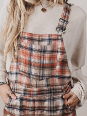 Person wearing a plaid dress with suspenders against a neutral background