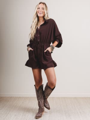 Woman wearing a brown romper and cowboy boots indoors.