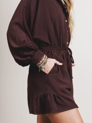 Brown romper worn by a person with colorful bracelets on a plain background
