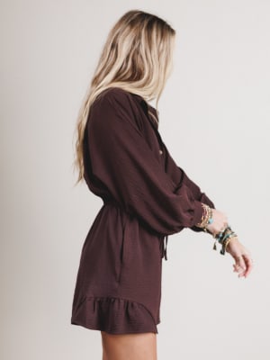 Woman wearing a brown romper with long sleeves and a ruffled hem on a plain background