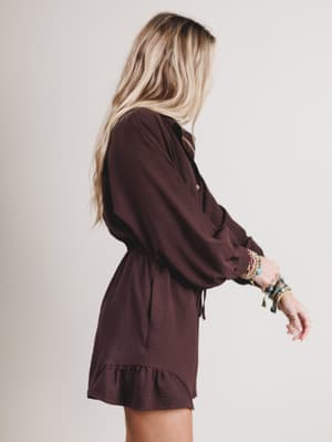 Woman wearing a brown romper with long sleeves and a ruffled hem on a plain background