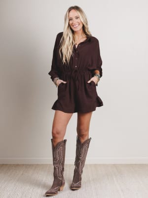 Woman wearing a brown romper and cowboy boots against a plain background