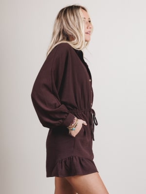Woman wearing a brown romper with long sleeves and a tie waist on a plain background
