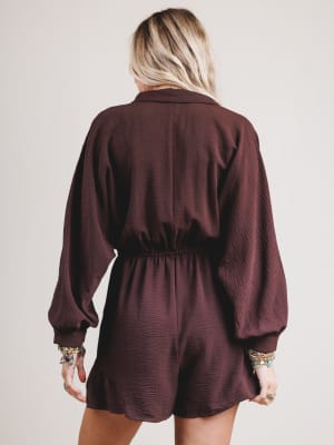 Person wearing a maroon romper with long sleeves on a plain background