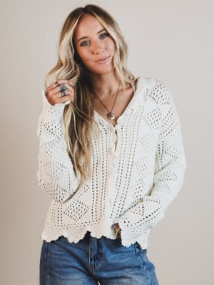 Woman wearing a white crochet sweater and blue jeans against a plain background