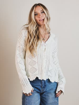 Woman wearing a white lace top and blue jeans against a plain background