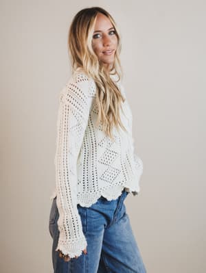 Woman wearing a white lace top and blue jeans against a plain background