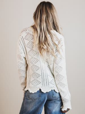 Person wearing a white lace cardigan and blue jeans against a plain background