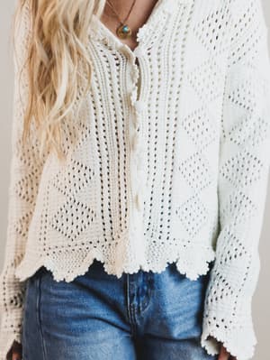 Person wearing a white crochet top and blue jeans against a neutral background
