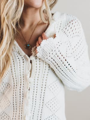 Close-up of a person wearing a white knitted sweater with a blurred background