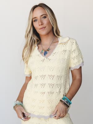 A soft, sun-washed crochet knit top in buttery yellow with a relaxed v-neck collar and layered boho jewelry — the kind of top that makes a Tuesday feel like a beach town.
