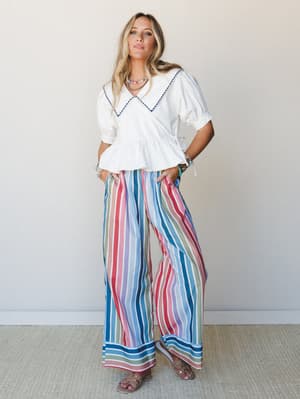 A bright, expressive summer outfit pairing a white peplum blouse with an oversized sailor collar against wide-leg multicolor stripe pants — the kind of look that feels equally at home on a boardwalk or at brunch.