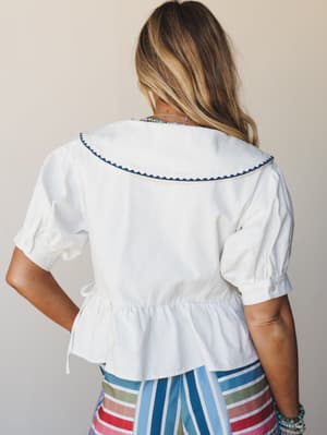 A back-view shot of a white peplum blouse with an oversized sailor collar trimmed in navy ric-rac, paired with colorful striped pants — playful and a little nostalgic, in the best way.