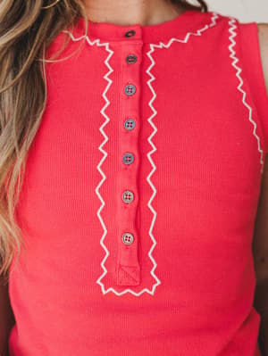 A close-up detail shot of a ribbed red tank with a retro-feel button-front placket framed in cream zigzag ric-rac trim — the kind of top that looks like it was made for warm afternoons and good company.