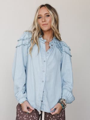 A light wash denim button-down top with ruffle yoke and shoulder details, styled with printed wide-leg pants and stacked boho jewelry — easy, expressive, and a little bit vintage in the best way.