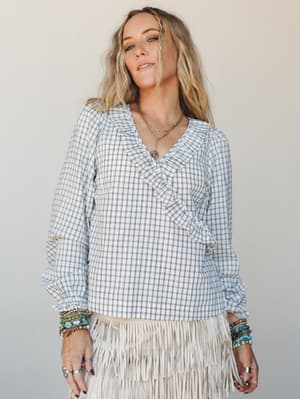 A relaxed, lived-in blouse in a soft plaid meets a cream fringe skirt — the kind of outfit that feels equally at home at a festival or a farmers market, styled with layered turquoise bracelets and gold chains that do all the talking.