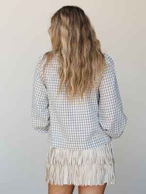 Shot from behind, this look pairs a relaxed plaid top with a tiered fringe mini skirt — the kind of outfit that feels effortless but clearly had a moment of intention behind it.