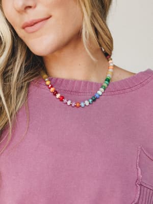 A multicolor beaded stone necklace sits at the collarbone against a washed mauve sweatshirt — the kind of piece that makes a Tuesday feel more intentional.