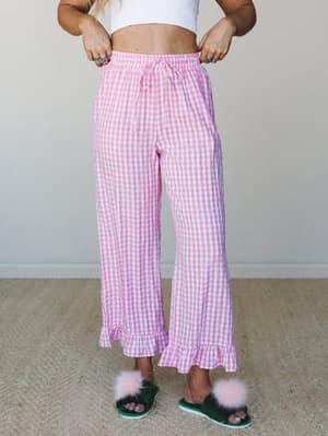 Pink gingham wide-leg pants with a ruffle hem and drawstring waist, styled with a white crop top and fuzzy slippers — playful and cozy with a sleepover-chic kind of energy.