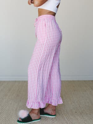 Pink gingham wide-leg pants with a ruffle hem and drawstring waist, styled with a white crop top and fuzzy slippers for a playful, cozy-at-home feel.