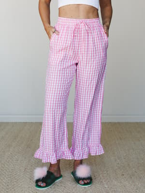 Pink gingham wide-leg pants with ruffle hems and a drawstring waist, styled with a white crop top and fluffy pom-pom slippers for a playful, cozy-at-home feel.