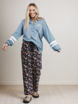 Woman wearing a blue long-sleeve shirt with a number design and floral pants against a plain background