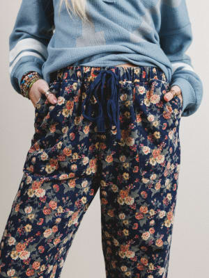 Person wearing a blue sweater and floral pants on a plain background