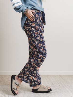 Person wearing navy floral pants and sandals on a light wooden floor.