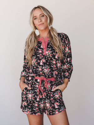 A matching floral top-and-shorts set in a dark black base with pink rose print — the kind of set that blurs the line between pajamas and an actual outfit, styled here with pearl earrings and pigtails like she absolutely could wear this to brunch.