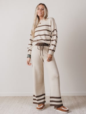 Woman wearing a striped sweater and pants set against a plain background