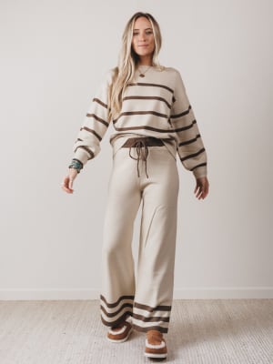 Woman wearing a beige and brown striped sweater and pants set on a plain background
