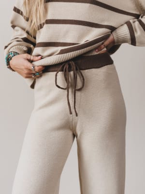 Person wearing a striped sweater and beige pants against a neutral background