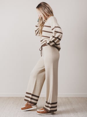Woman wearing a striped sweater and pants set with brown shoes on a plain background