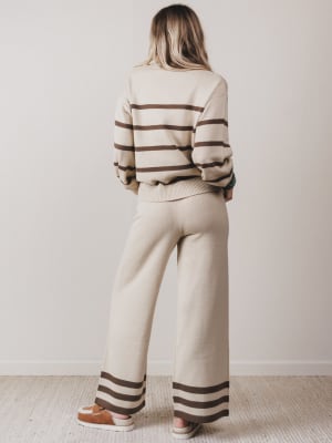 Person wearing a beige and brown striped sweater and pants set against a plain background