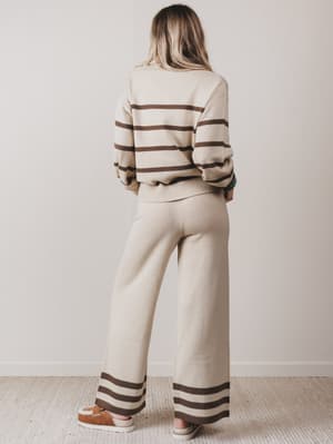 Person wearing a beige and brown striped sweater and pants set against a plain background